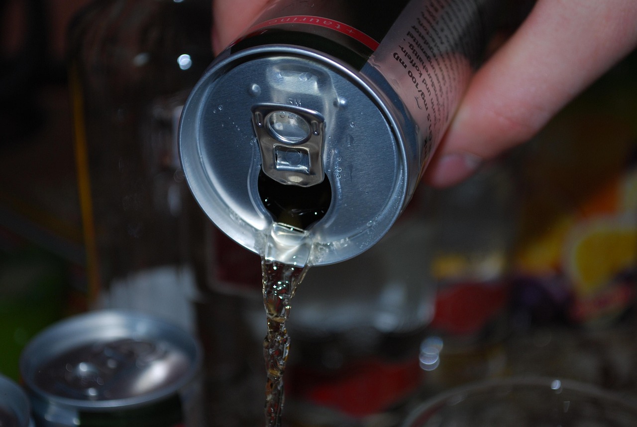 Une main verse le liquide contenu dans une canette de boisson énergisante avec le fond flou